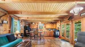 Interior de una cabaña de madera con comedor, cocina y sofá.