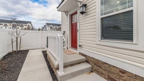 A residential building with a red door, white exterior, and a small porch with steps. - New Townhome Steps from the Beach (Ocean City)