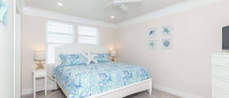 A bedroom with a bed, a ceiling fan, a nightstand with a lamp, and wall art.