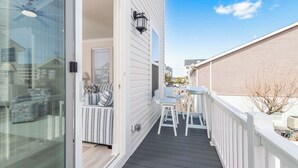 A balcony with a table and chairs, a window with blinds, and a door leading to the interior. - New Townhome Steps from the Beach (Ocean City)