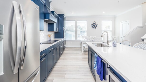 A modern kitchen with a stainless steel refrigerator, dark blue cabinets, a white countertop, and a window with blinds. - New Townhome Steps from the Beach (Ocean City)