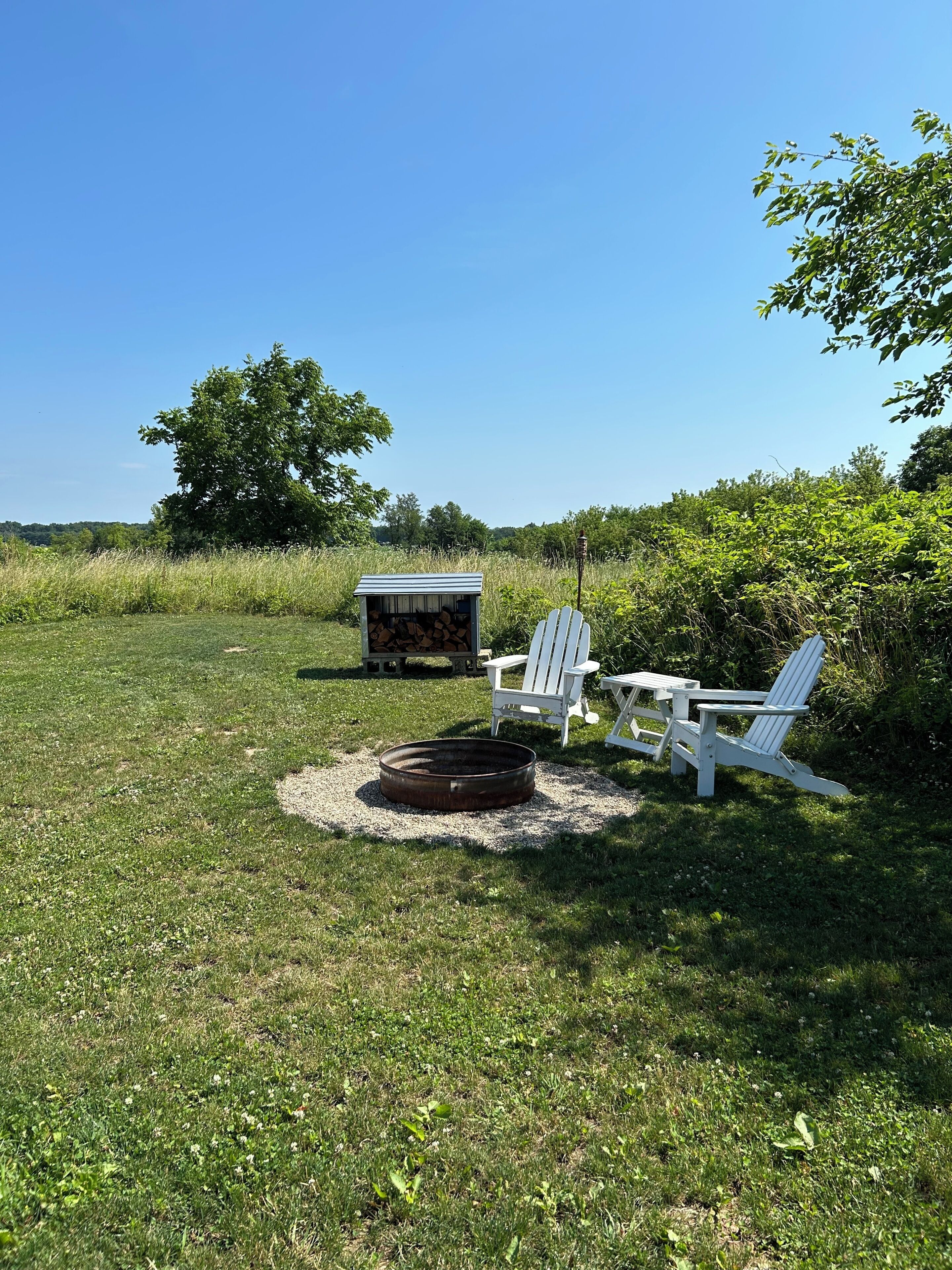 Un espace extérieur verdoyant avec un foyer, deux fauteuils Adirondack et un petit abri de jardin.