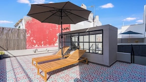 Terraço no telhado com duas poltronas de madeira, um guarda-sol grande e piso estampado.