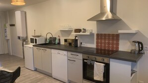 A modern kitchen with white cabinetry, a stainless steel range hood, a built-in oven, and a black countertop.