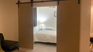 A room with a bed, a chair, a lamp, and a sliding door leading to another room.