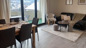 A dining area with a table set for four, a sofa, and a chair with a view of a snowy landscape through a large sliding glass door.