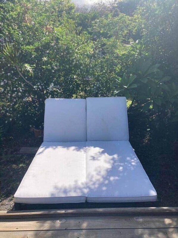 Un matelas blanc avec deux oreillers, posé sur une plateforme en bois, le tout entouré d’un feuillage vert et luxuriant.