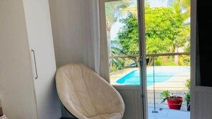 A bedroom with a bed, a chair, a view of a swimming pool, and a door leading outside.