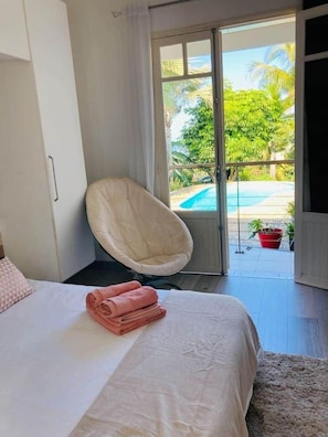 A bedroom with a bed, a chair, a view of a swimming pool, and a door leading outside.