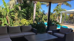 A covered outdoor seating area with a pool in the background.