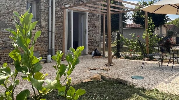 Un edificio de piedra con una pérgola de madera y asientos exteriores.