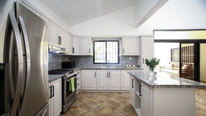 Uma cozinha moderna com armários brancos, bancadas de granito, eletrodomésticos de aço inoxidável e uma grande janela que traz luz natural.