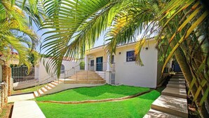 Uma casa com gramado bem cuidado, uma escadaria que leva à entrada e um céu claro.