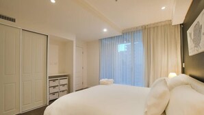 A bedroom with a large bed, a wardrobe, a bedside table, and a window with curtains. - Amyra Residences on Rowlands Place - Unit 803 (Adelaide)