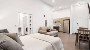 Ein modernes Hotelzimmer mit Bett, einer Couch, einem Esstisch und einer Küchenzeile.