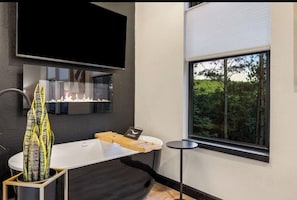 Une salle de bain moderne avec une baignoire, un grand miroir et une fenêtre donnant sur les arbres.