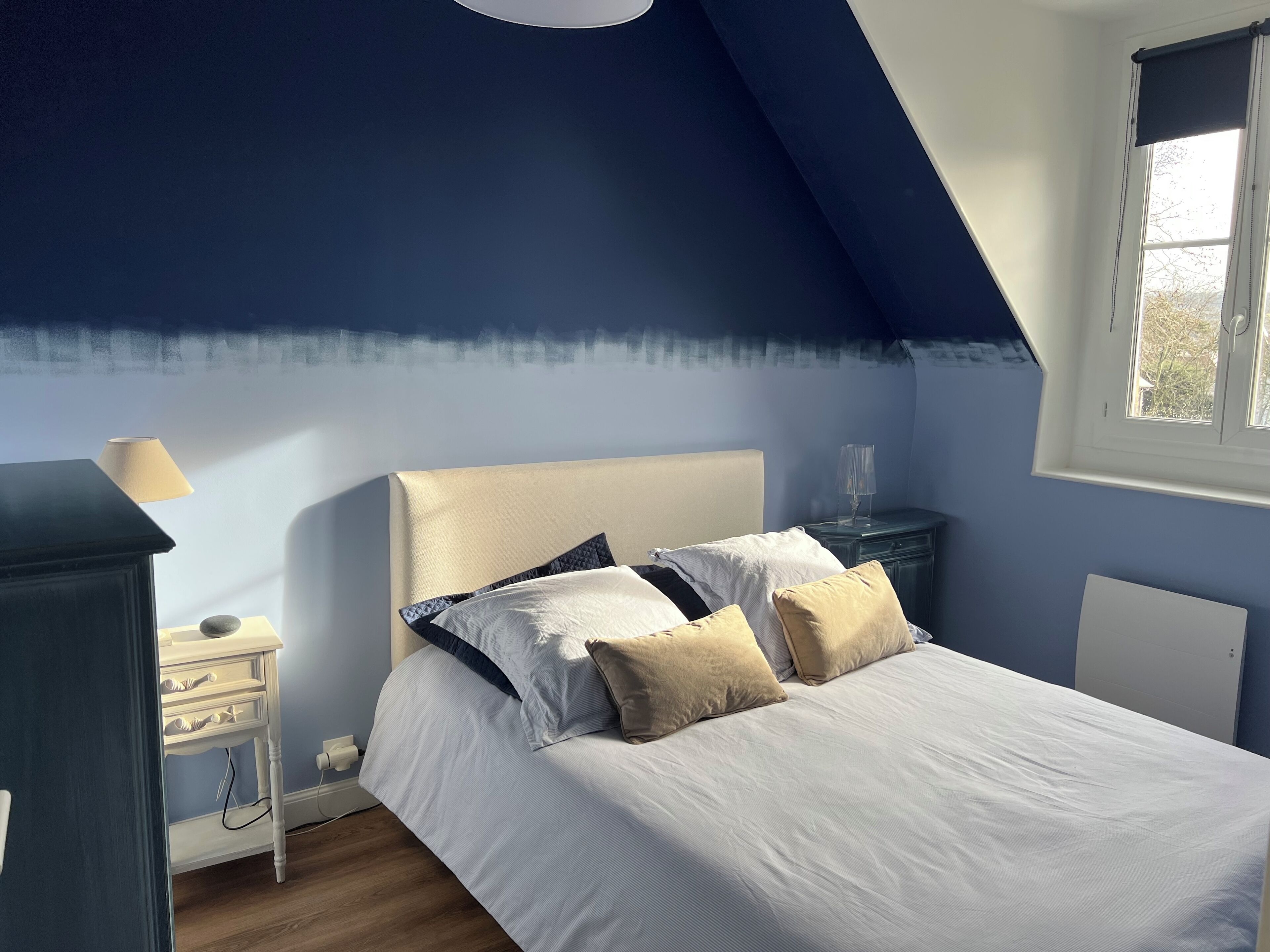 A bedroom with a bed, bedside table, lamp, and a window with a view of trees.