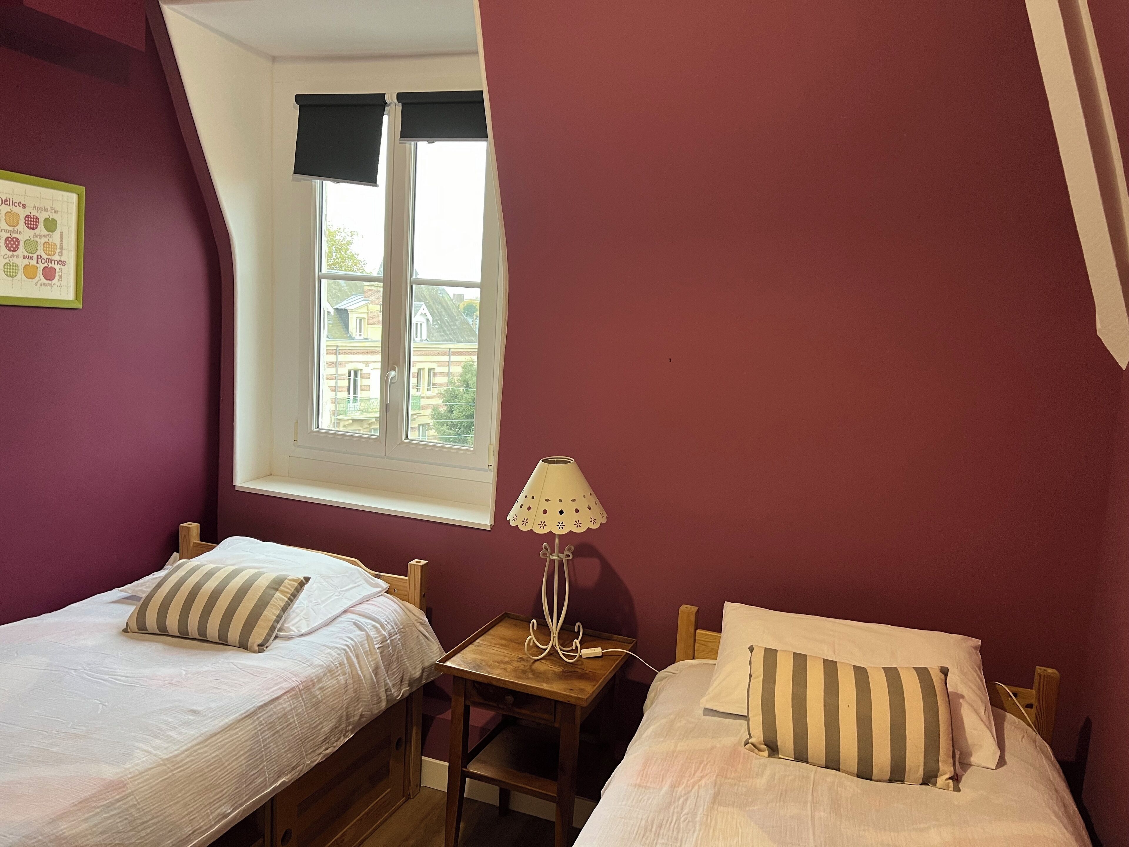 Un dormitorio con dos camas, una mesita de noche con lámpara y una ventana con persianas.