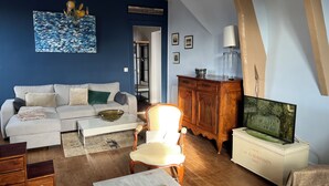 A living room with a white sofa, a wooden cabinet, a television, and a painting on the wall. - Cabourg fan (Cabourg)