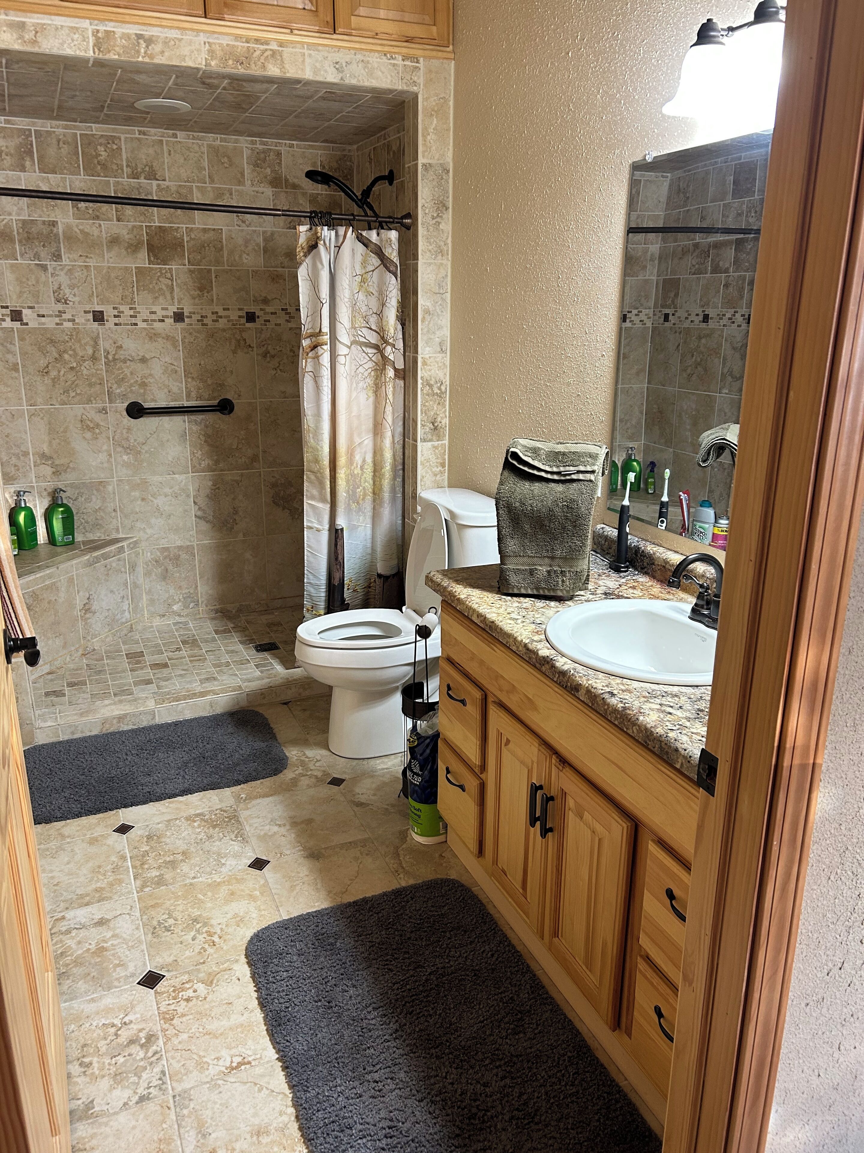 Een badkamer met een douche, toilet, wastafel en houten kasten.