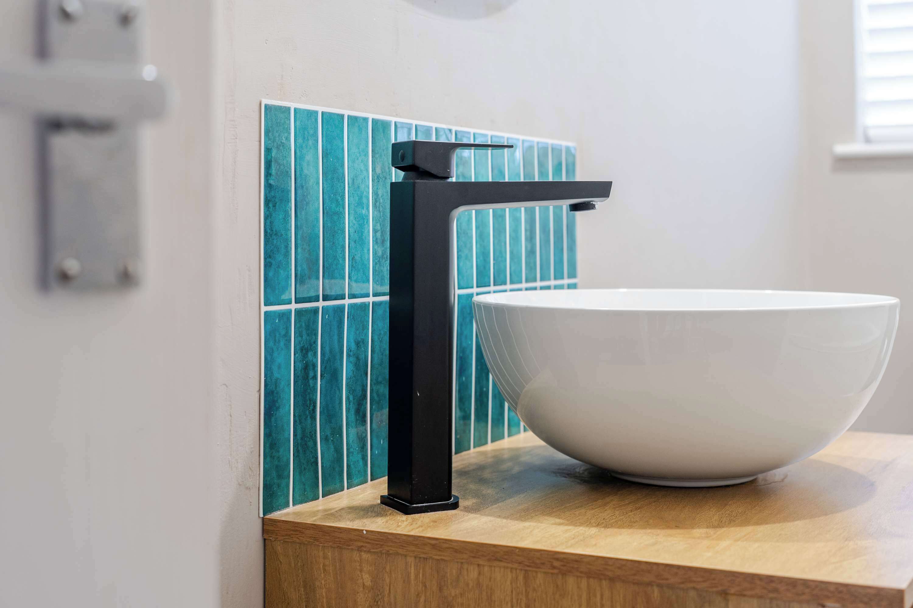 Un baño con lavamanos blanco, grifo negro y azulejos verde azulado.