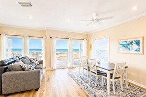 A room with a sofa, dining table, chairs, a ceiling fan, and large windows with a view of the beach. - Barbara Ann's Happy Place (Eastpoint)