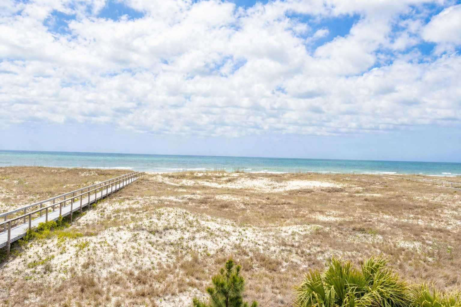 A beach with a wooden boardwalk leading to the water, sandy dunes, and sparse vegetation.