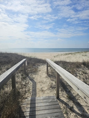 Een houten looppad dat naar een zandstrand leidt, onder een heldere lucht.