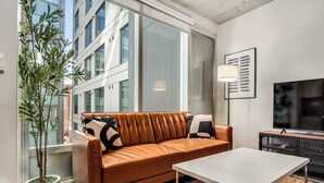 A modern living room with a leather sofa, a white coffee table, a large window, and a television.