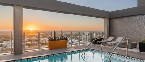 Ein Dachpool mit Blick auf die Stadt bei Sonnenuntergang, Liegestühle und ein Pflanzgefäß mit Pflanzen.