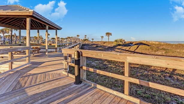A wooden boardwalk leading to a covered pavilion with benches and picnic tables, surrounded by dunes and palm trees. - Amelia Island 3 BR Ocean Park Beach Getaway (Fernandina Beach)