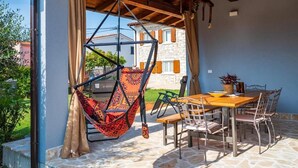 A patio with a hanging chair, a table with chairs, and a view of a stone building. - Charming House With Garden and BBQ in Galizana (Vodnjan)