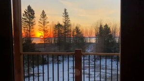 A wooden deck with a metal railing overlooking a snowy landscape and a sunset.