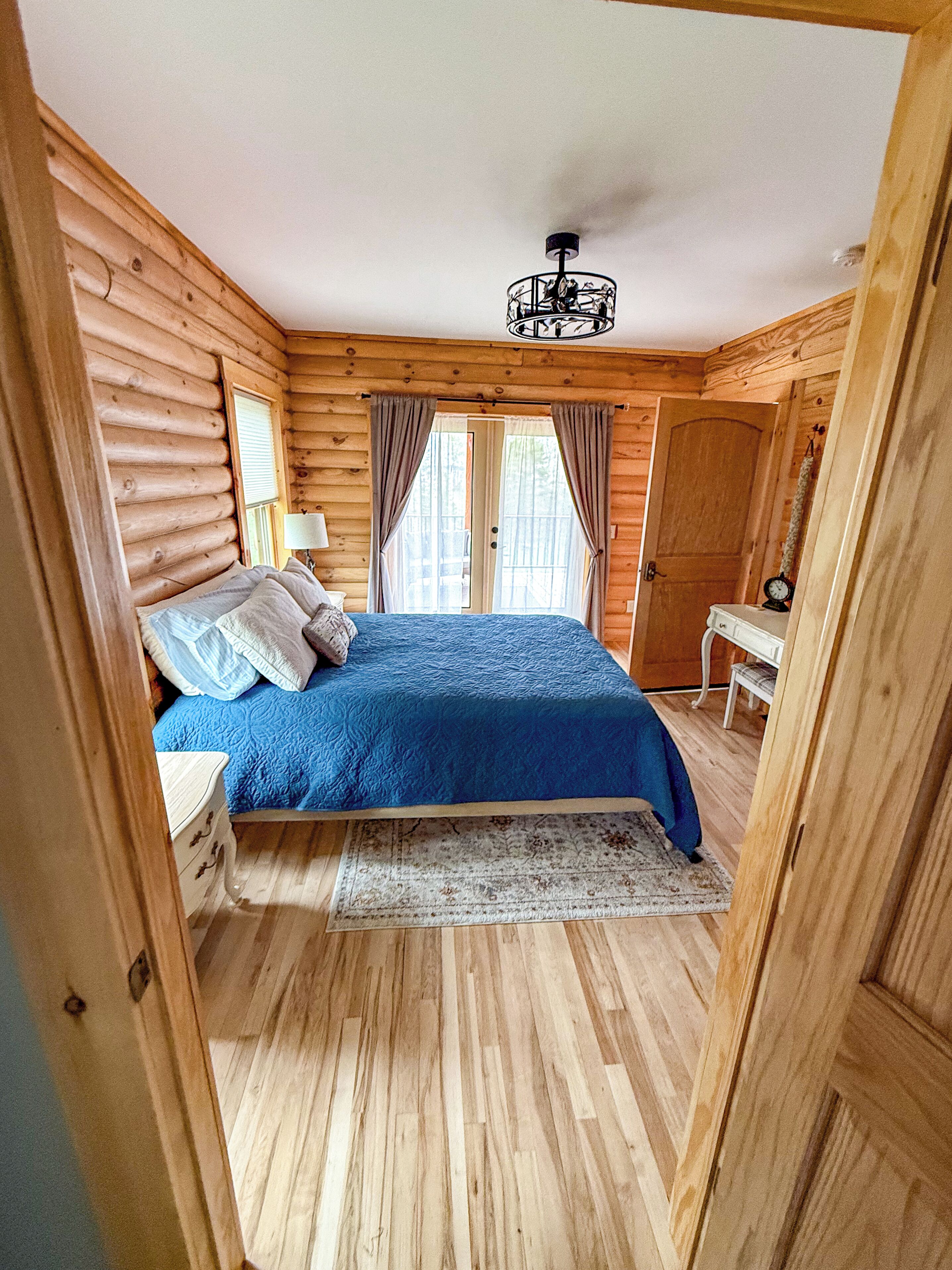 A log cabin bedroom with a bed, a nightstand, a lamp, and a wooden door.