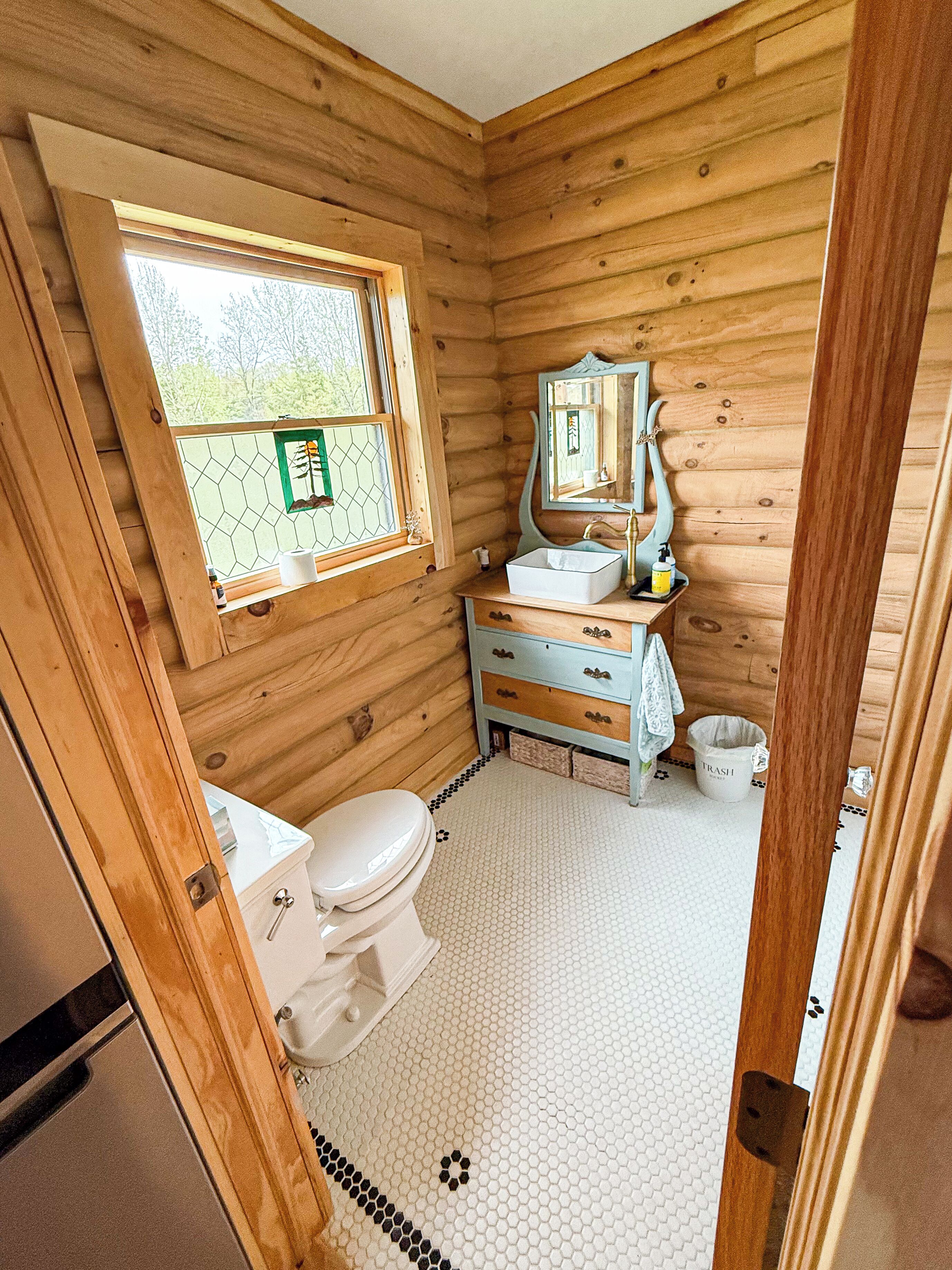 A wooden cabin bathroom with a toilet, sink, and window.