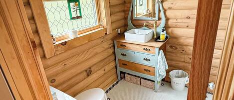 A wooden cabin bathroom with a toilet, sink, and window.