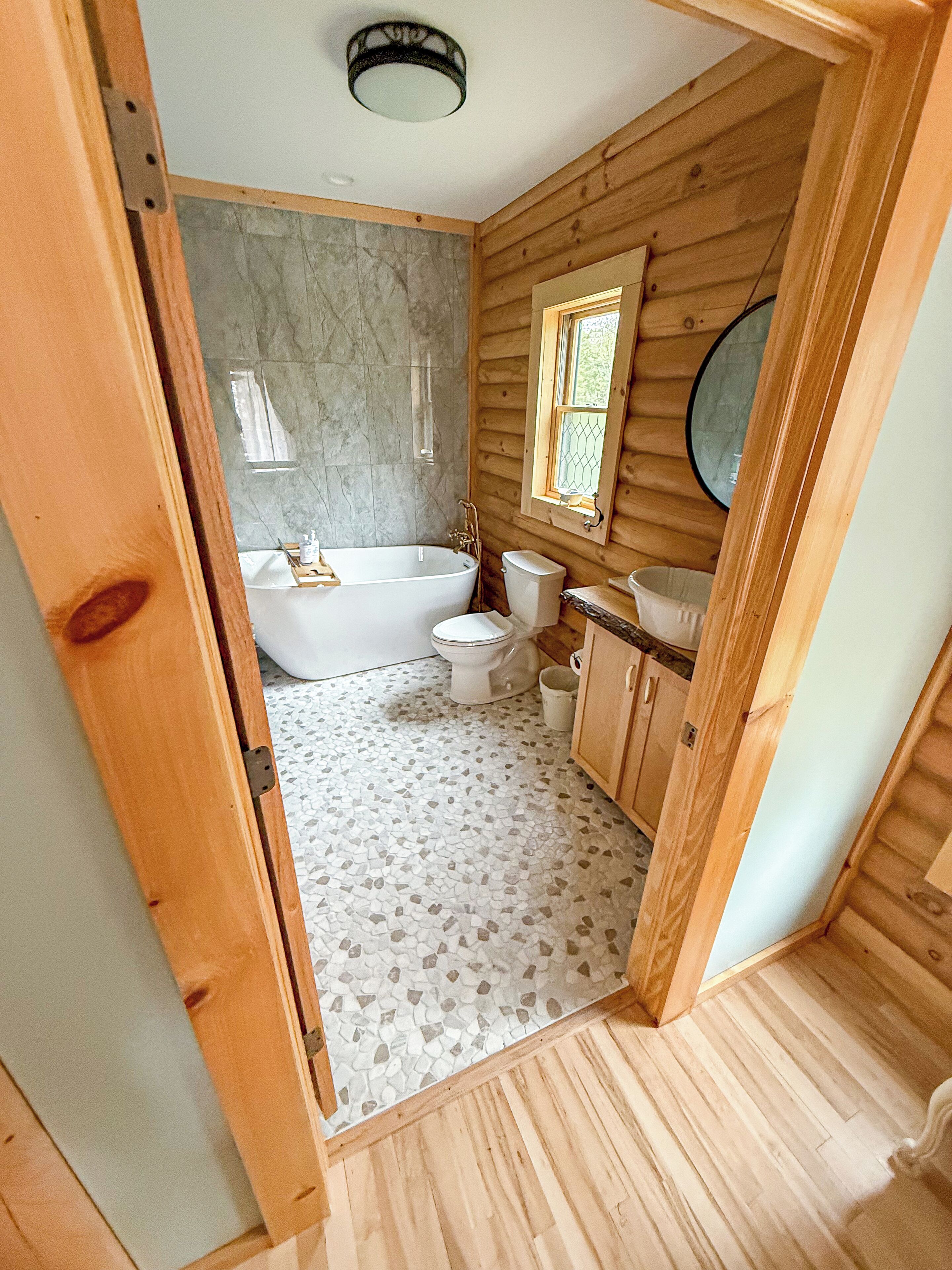 Baño de cabaña de madera con bañera, inodoro y lavamanos.