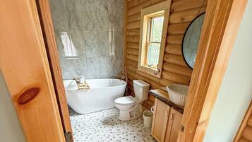 A wooden cabin bathroom with a bathtub, toilet, and sink.