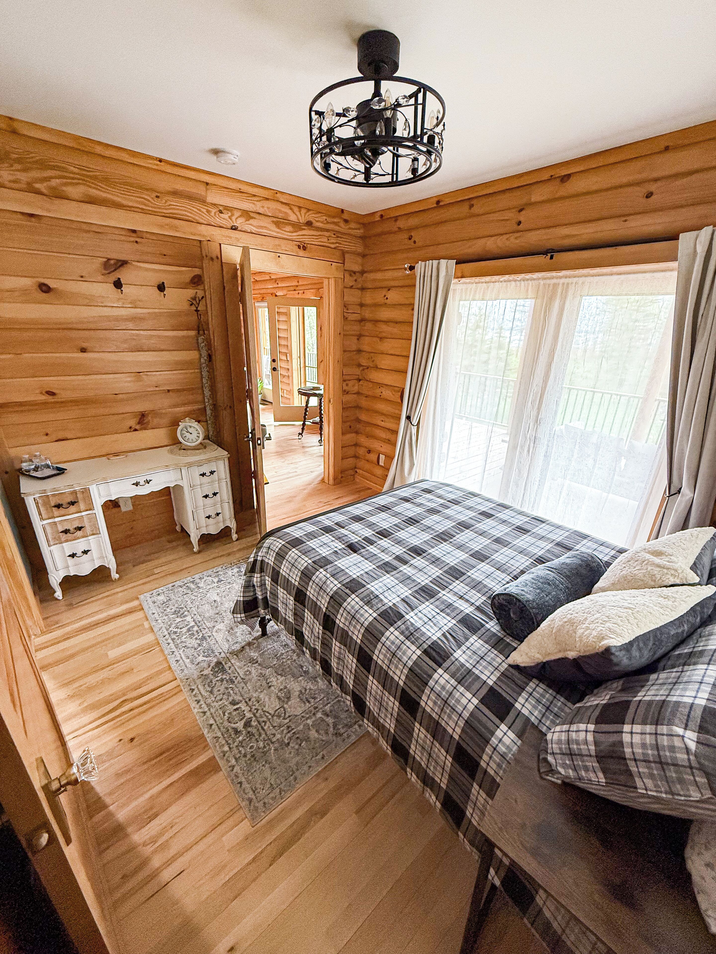 A wooden cabin bedroom with a bed, a desk, and a chair.