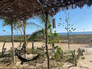 Relax in a serene thatched-roof gazebo surrounded by cacti and small trees.