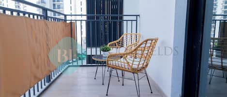 A balcony with two wicker chairs, a small table, and a potted plant.