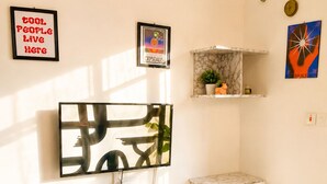 Una sala de estar moderna con un sofá blanco, una mesa de centro, un televisor montado en la pared y un estante con objetos decorativos.