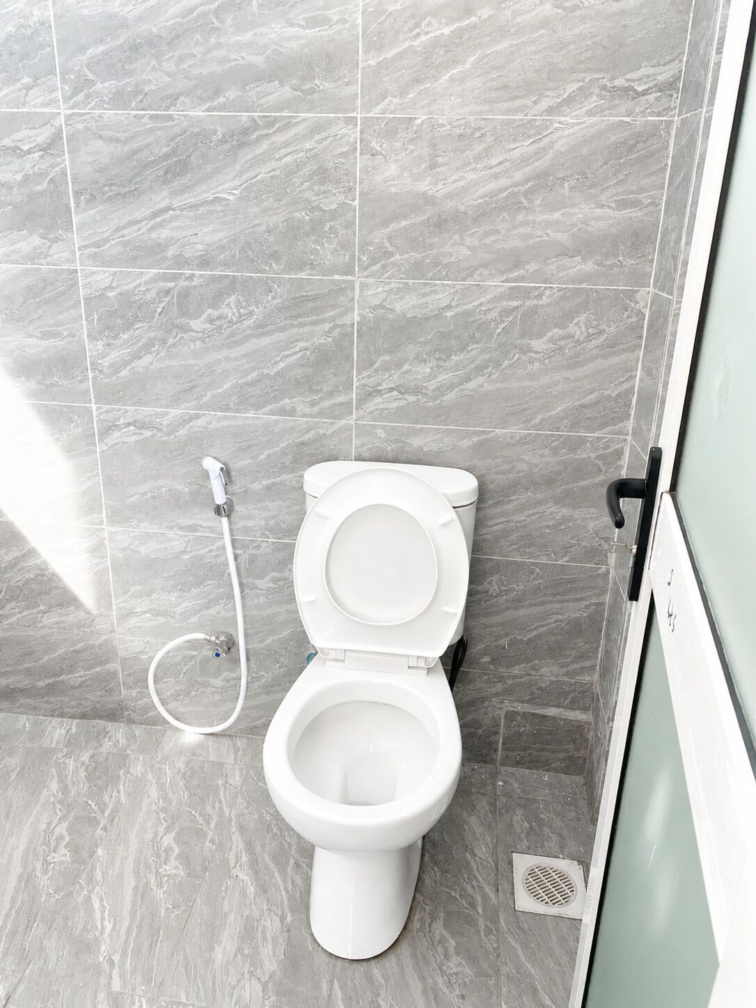 Een moderne badkamer met een wit toilet, een handdouche en een vloerafvoer.