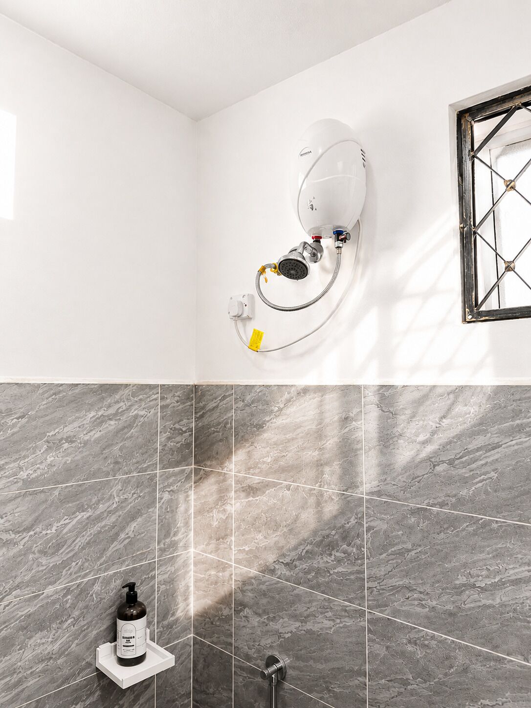 Un bagno con doccia a parete, asciugatore d'aria e una bottiglia di shampoo su uno scaffale.