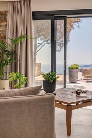 A modern living room with a view of the sea, a wooden table, and potted plants. - Pnoe Villas Syros (Syros)