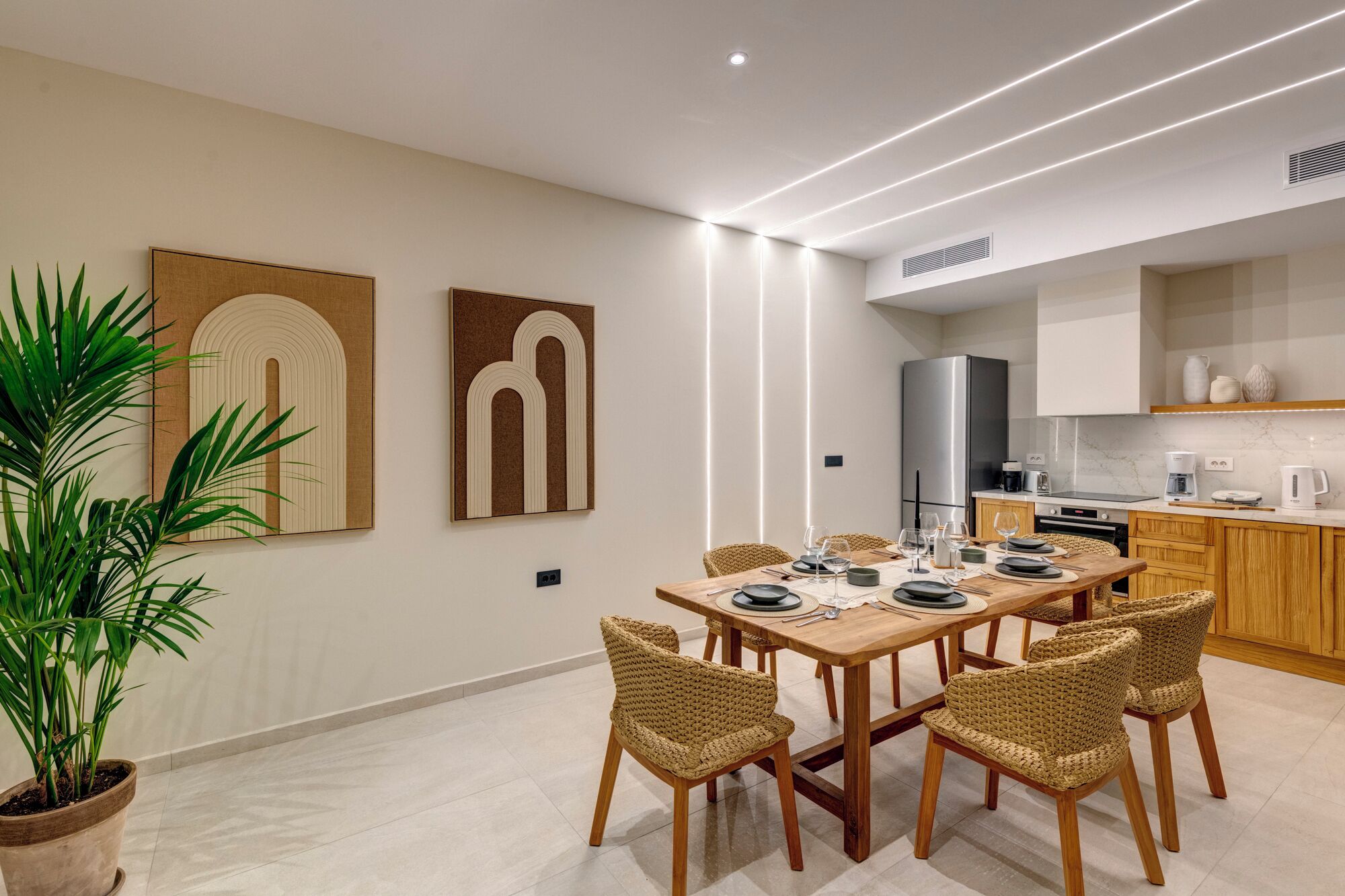 A modern dining area with a wooden table, woven chairs, and a potted plant.