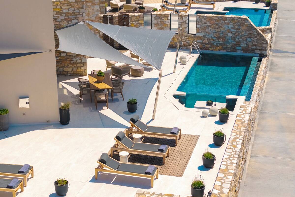 A rooftop pool area with lounge chairs, a table, and potted plants.