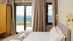 Une chambre d’hôtel avec un grand lit, une armoire en bois et une vue sur la mer, visible à travers une porte vitrée.