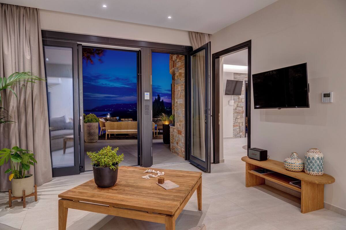 A modern living room with a wooden coffee table, a flat-screen TV, and a stone wall.
