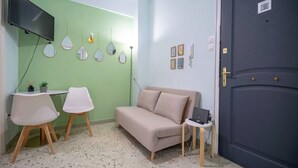 A room with a green wall, a beige sofa, two white chairs, a small table with a laptop, and a dark door.